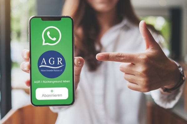 Das Bild zeigt einen Handybildschirm mit dem AGR-WhatsApp Kanal und eine Frau im Hintergrund.